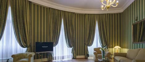 A spacious living room with a television, two armchairs, a sofa, and a chandelier.