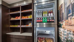 A kitchenette with a refrigerator stocked with beverages and snacks, and a wall-mounted shelf with packaged goods. - La Quinta Inn by Wyndham Everett (Everett)