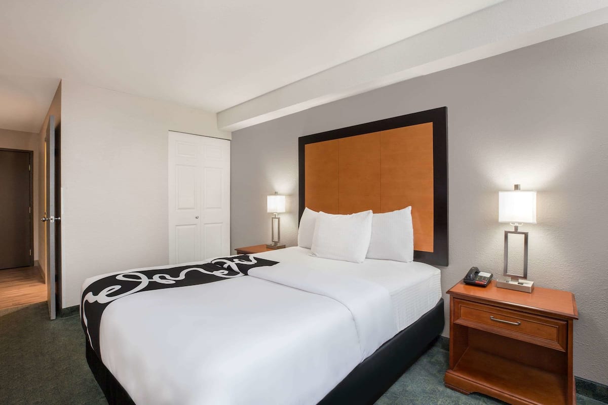 A hotel room with a large bed, a wooden nightstand with a lamp, and a door.
