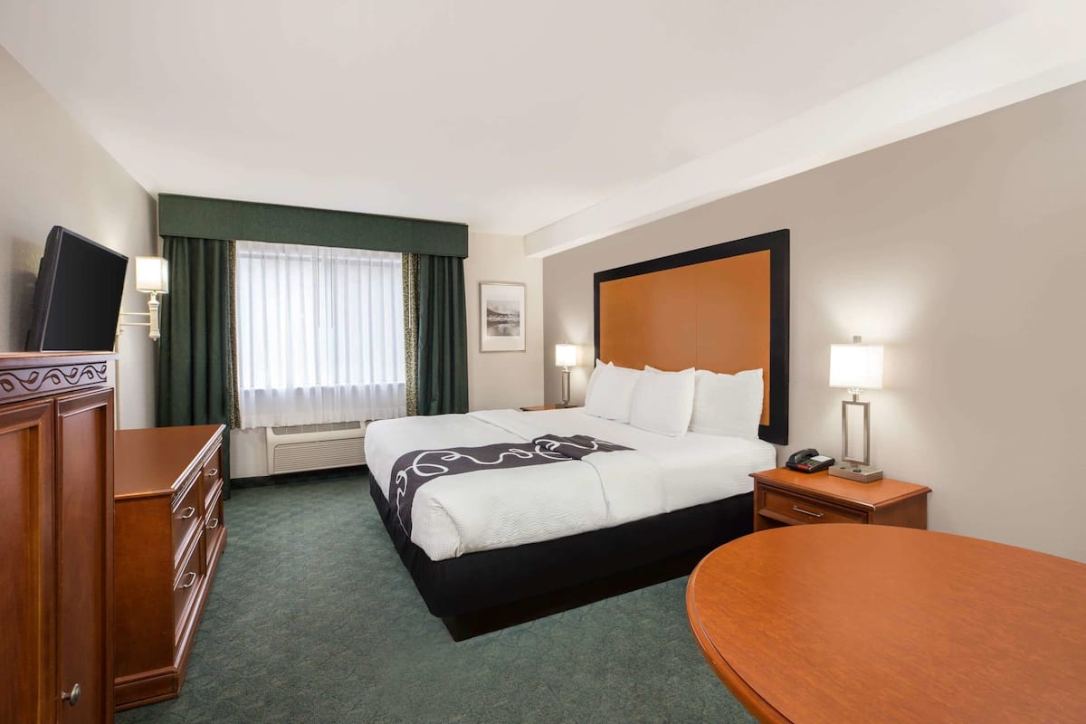 A hotel room with a large bed, a desk, a chair, a dresser, a TV, and a window with curtains.