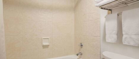 A bathroom with a bathtub, a toilet, and a towel rack with folded towels.