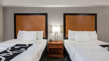A hotel room with two beds, a nightstand with a lamp, and a small table.