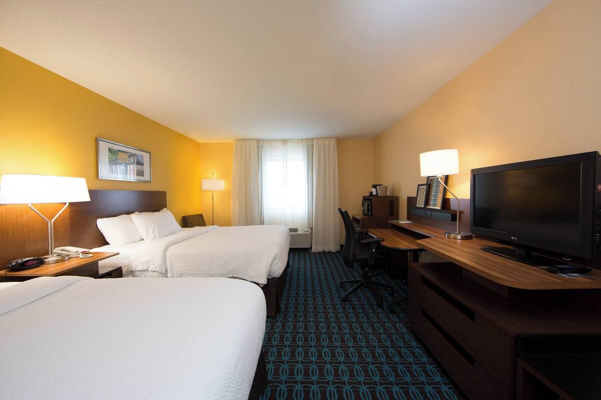 A hotel room with two beds, a desk with a TV, and a window with curtains.