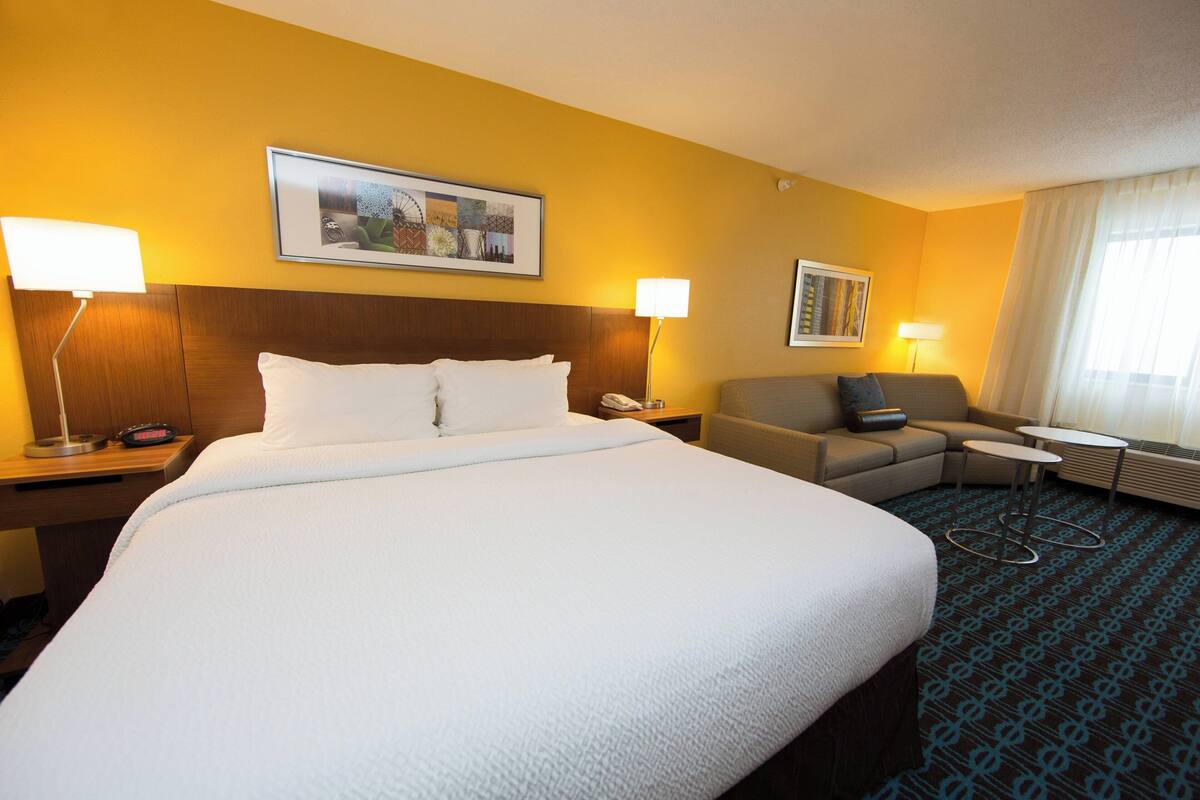A hotel room with a large bed, a sofa, a small table, and two lamps.