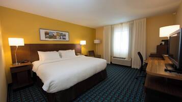 A hotel room with a large bed, two bedside tables with lamps, a desk with a computer and TV, and a window with curtains.