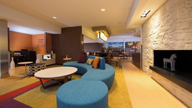 A modern lounge area with a stone fireplace, a blue sofa, and a small table. - Fairfield Inn & Suites by Marriott Burlington (Burlington)