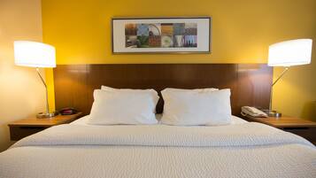 A hotel room with a large bed, two bedside tables, a framed artwork above the bed, and two lamps on the nightstands.