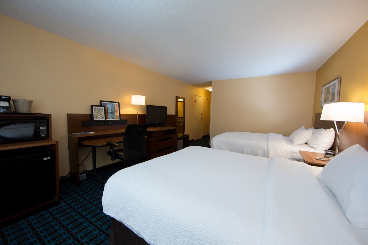 A hotel room with two beds, a desk with a computer, a microwave, and a TV.