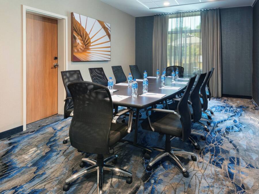 A conference room with a long table, multiple chairs, water bottles, and a large window with curtains.