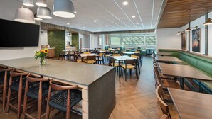 Un restaurante moderno con una isla central, varias zonas de estar y un amplio ventanal que proporciona luz natural.