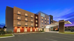 Un hotel de varios pisos con un letrero llamativo, una entrada cubierta y un estacionamiento.