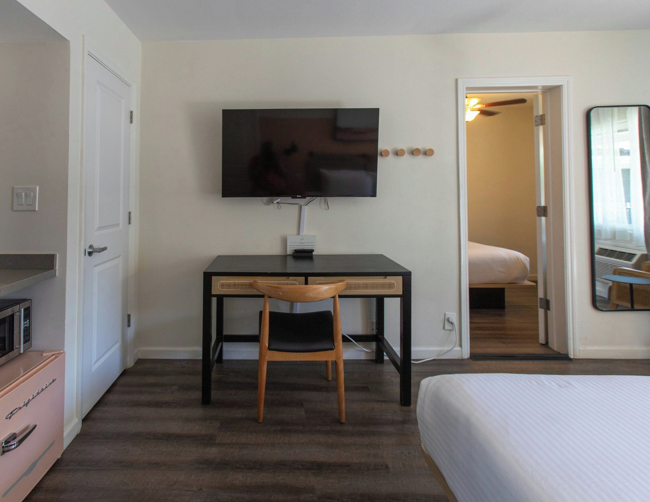 A hotel room with a bed, a desk with a chair, a television, and a mirror.