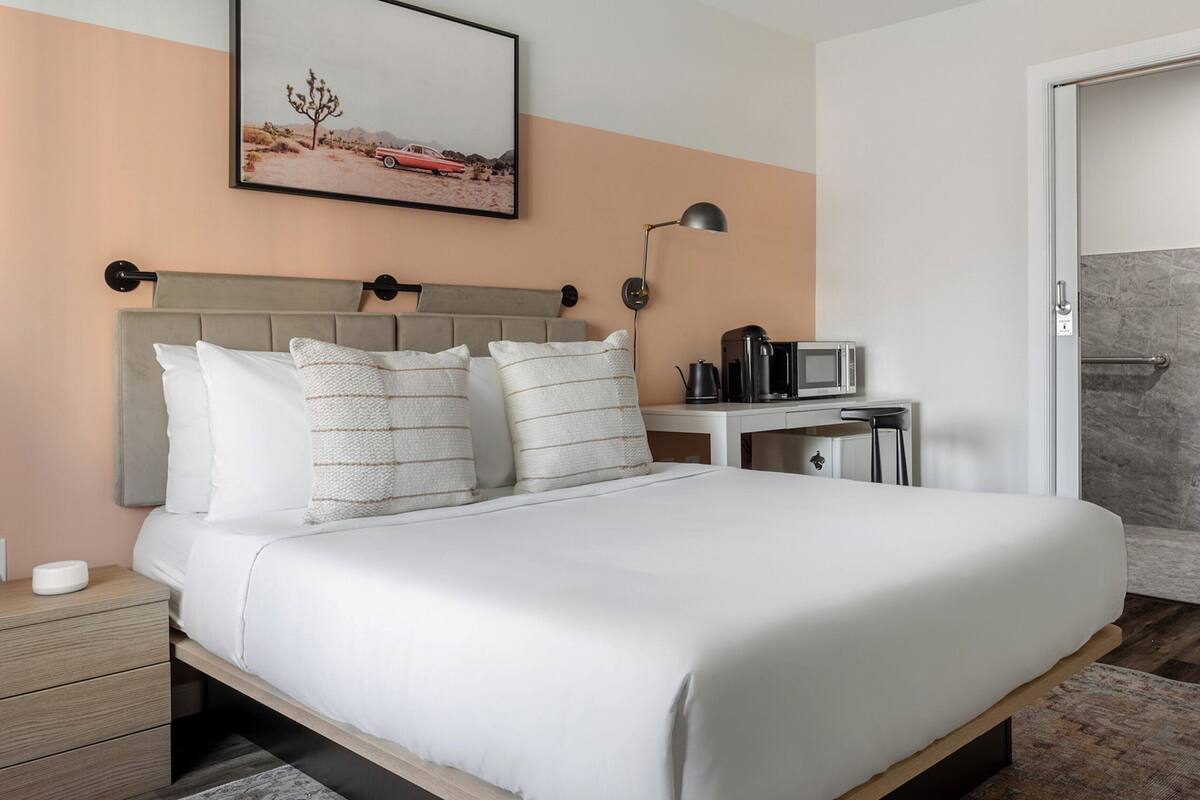 Una cama bien tendida con ropa blanca, cabecera y dos mesitas de noche con lámparas.