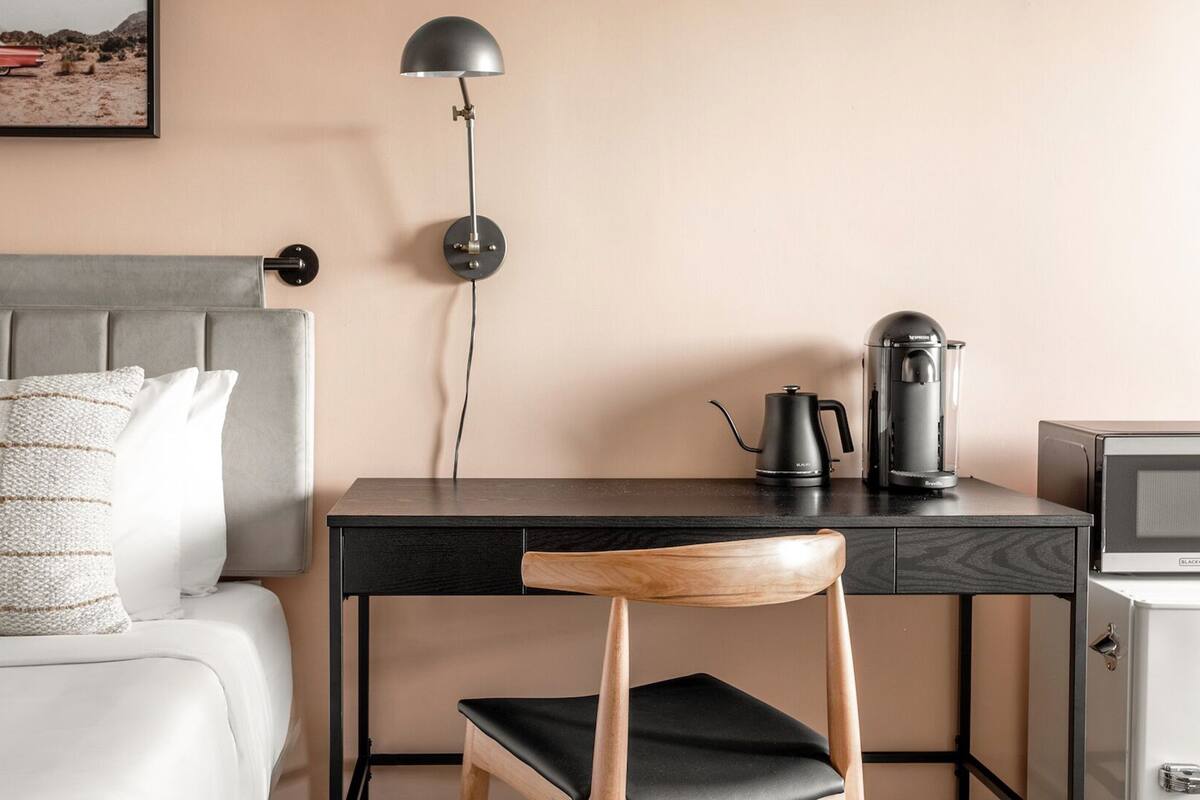 Un dormitorio con cama, escritorio, silla, lámpara, cafetera y televisión.