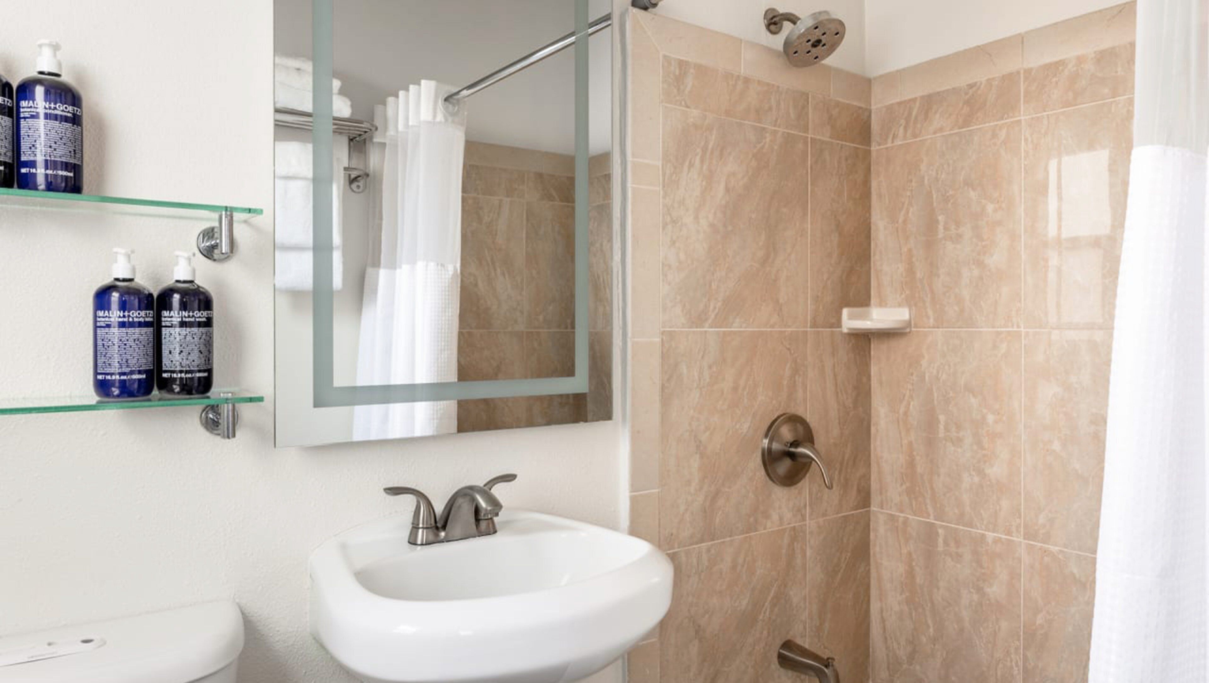 A bathroom with a sink, mirror, shower, and shelves with toiletries.