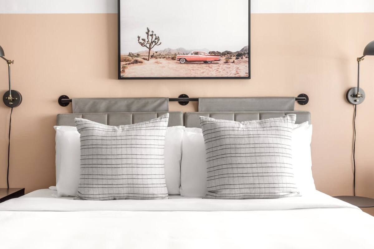 Una cama bien hecha con dos almohadas, cabecero y dos lámparas de noche.