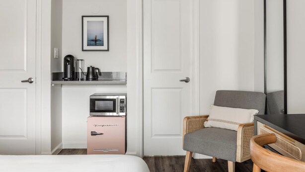Ein Hotelzimmer mit einem Bett, einem Sessel, einer Mikrowelle, einer Kaffeemaschine und einem gerahmten Bild an der Wand.