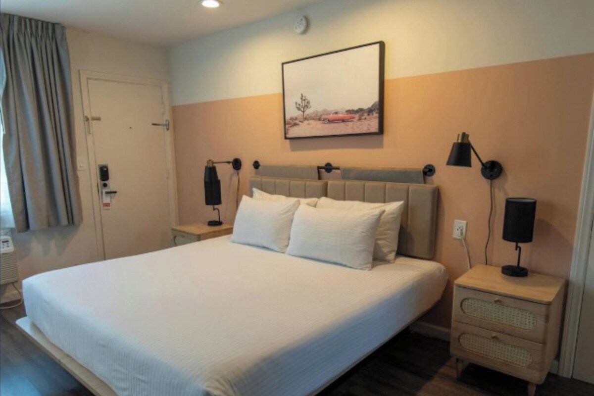 A hotel room with a large bed, a nightstand with a lamp, a wall-mounted picture, and a door with a lock.