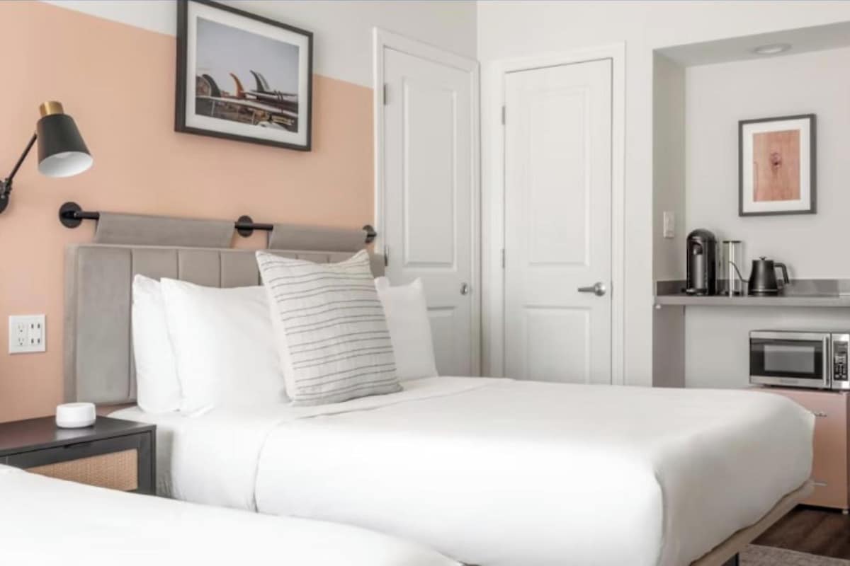 A hotel room with a bed, bedside lamp, and a kitchenette with a microwave.