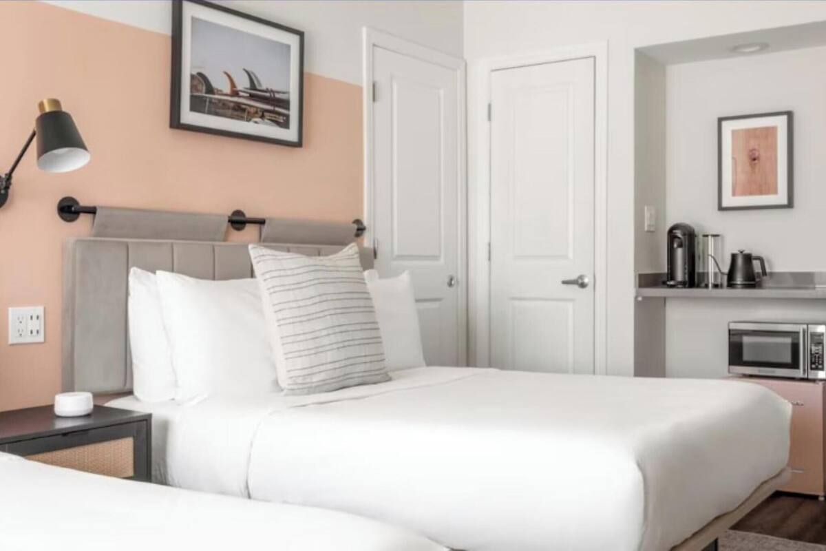 Habitación de hotel con cama, lámpara de noche y una kitchenette con microondas.