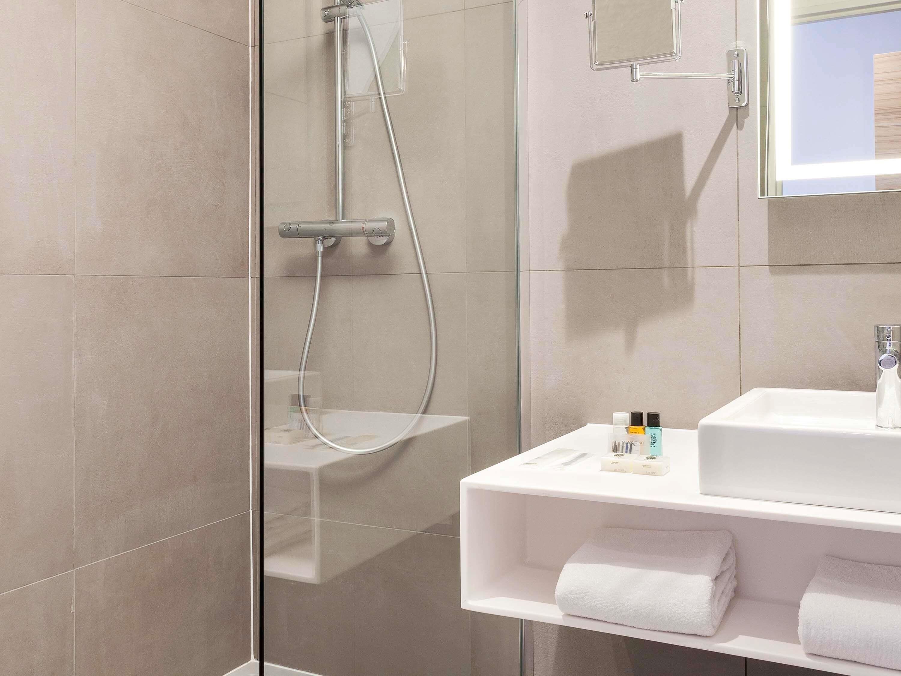 A modern bathroom with a glass shower enclosure, a white sink, and a mirror above it.