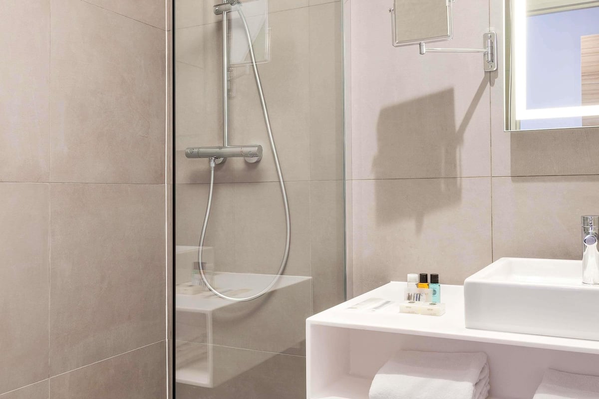 A modern bathroom with a glass shower enclosure, a white sink, and a mirror above it.