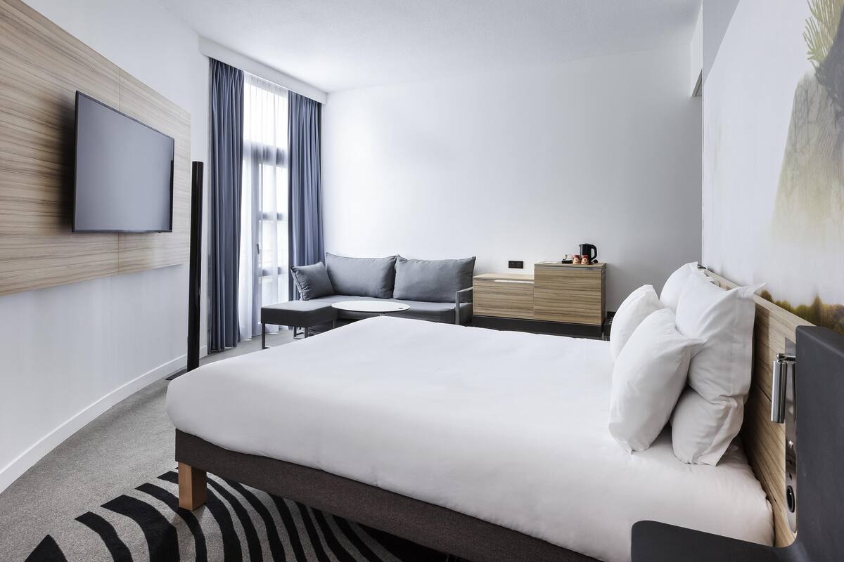 Habitación de hotel moderna con cama, escritorio, televisión de pantalla plana y un amplio ventanal con cortinas.