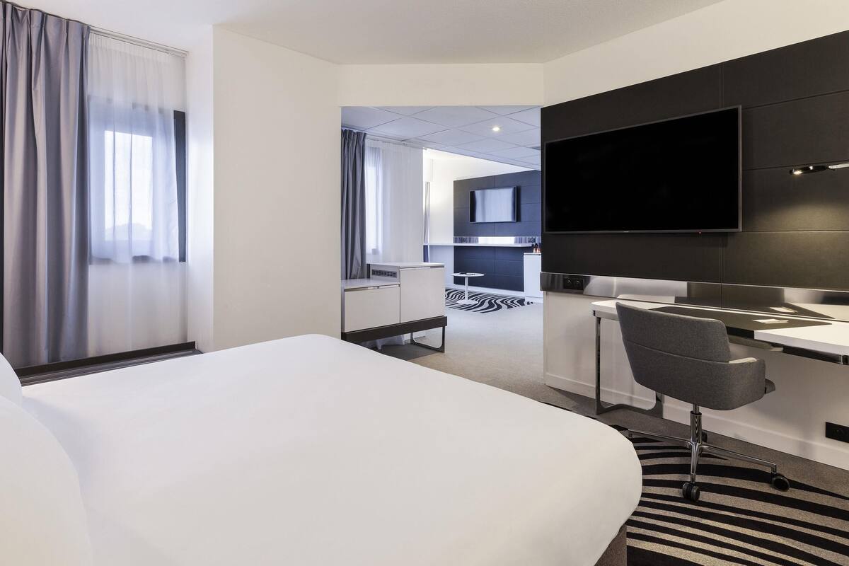 Una habitación de hotel con cama, escritorio, silla, televisor y una kitchenette al fondo.