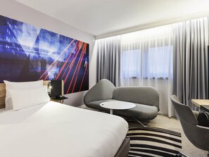 Habitación de hotel con cama, sofá, una mesita y un cuadro abstracto grande en la pared.