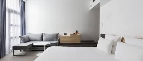 Una habitación de hotel moderna con una cama grande, un sofá, una pequeña mesa y un aparador de madera.