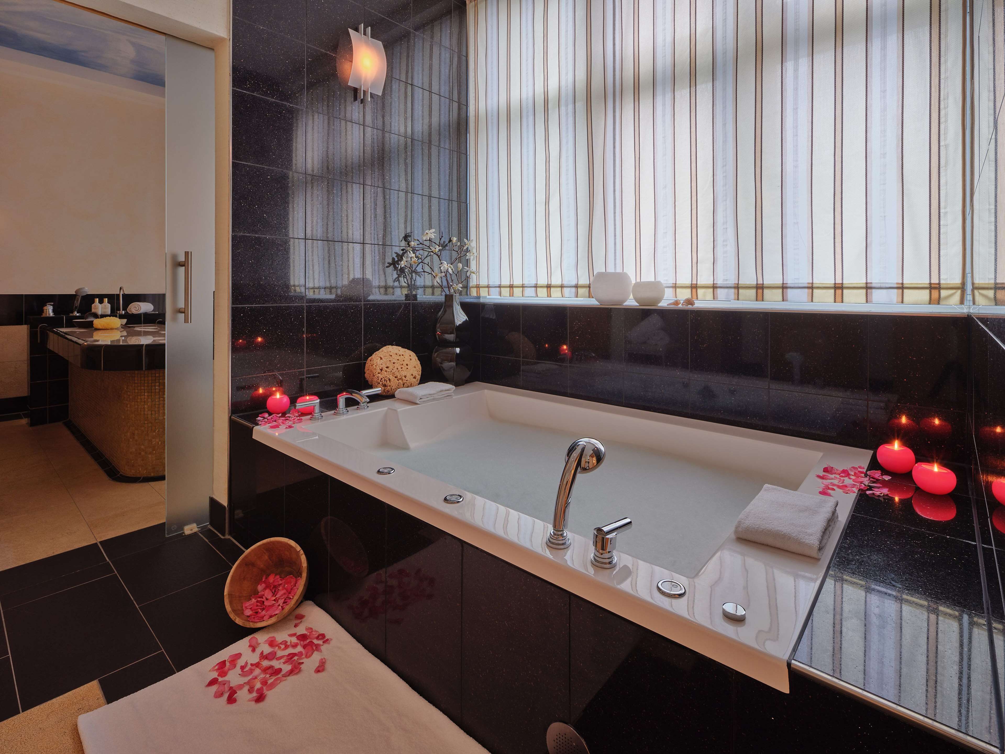 Ein modernes Badezimmer mit einer großen Badewanne, einem Waschtisch mit Spiegel und einem Fenster mit Vorhängen.