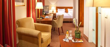 A hotel room with a bed, a desk with a computer, a chair, a sofa, and a coffee table with a plant.