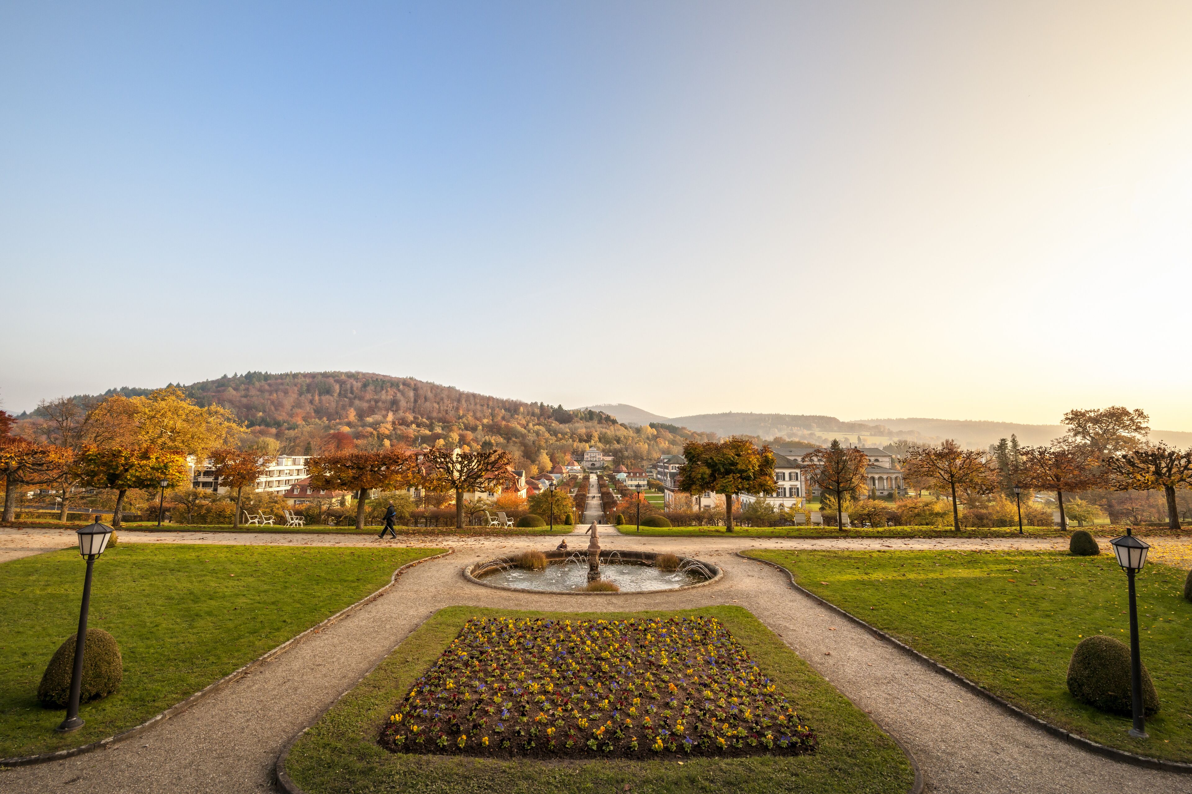 Un parque con una fuente, un sendero y vistas a un pueblo al fondo.