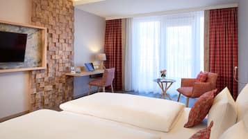 Hotelkamer met een groot bed, twee fauteuils, een bureau met een laptop, een aan de muur bevestigde televisie en een raam met gordijnen.