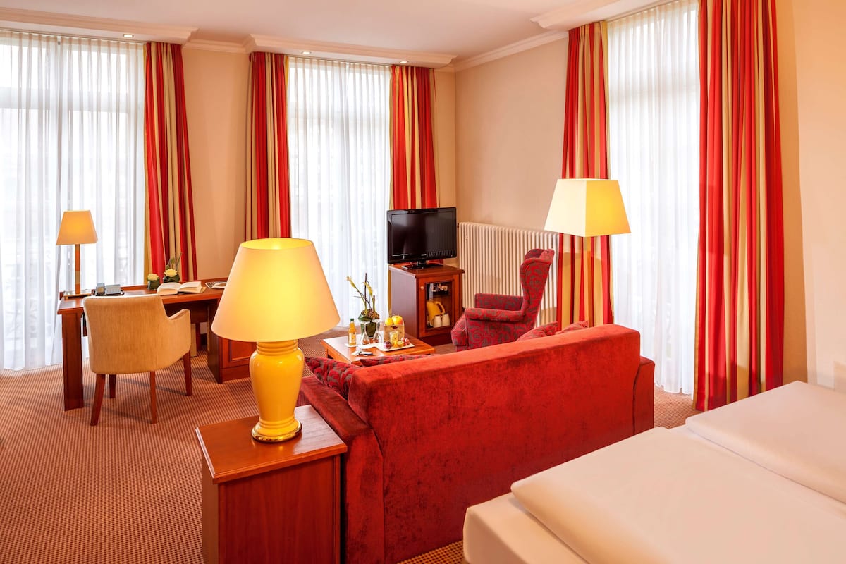 Une chambre d’hôtel avec un canapé rouge, un lit, une télévision, un bureau avec une lampe et une chaise.