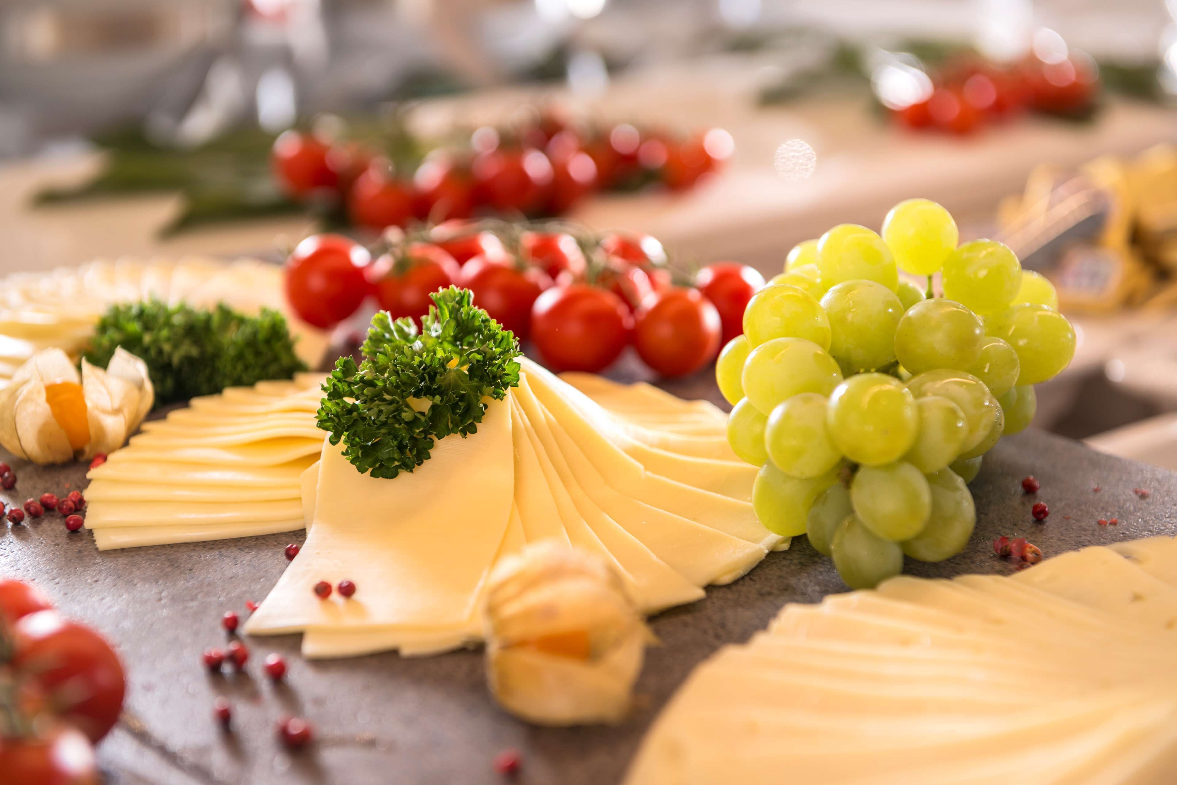 A cheese board with various cheeses, grapes, and cherry tomatoes.