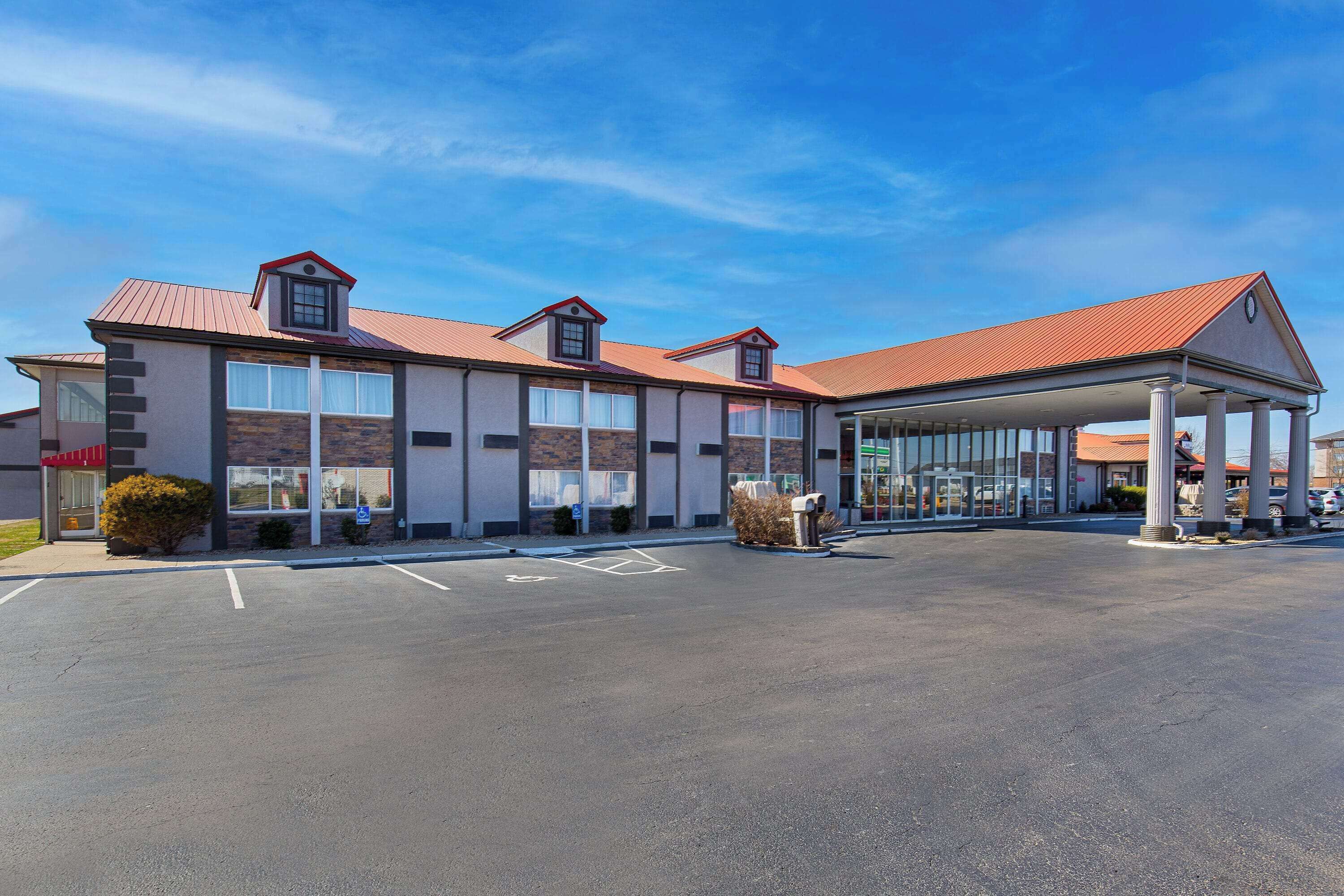 A modern hotel with a covered entrance, large windows, and a parking lot.