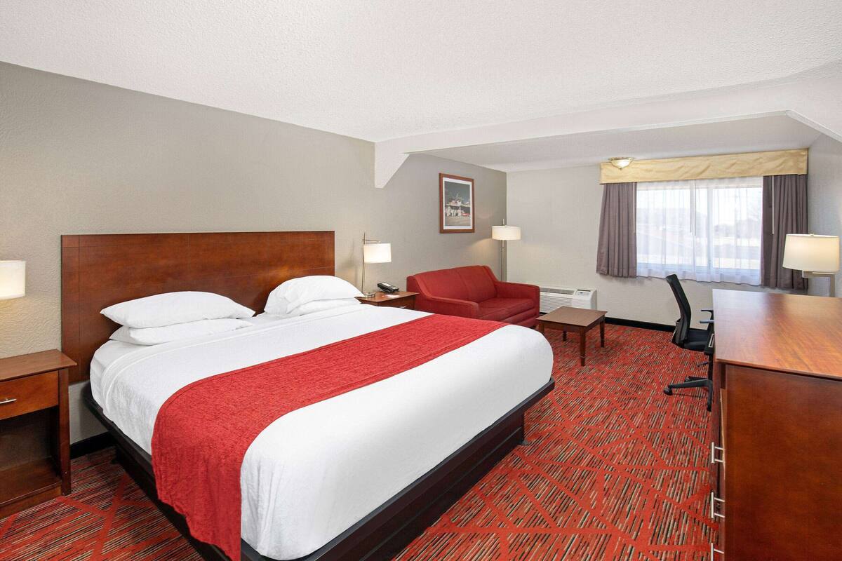 Ett hotellrum med en stor säng, ett skrivbord, en stol och ett fönster med gardiner.