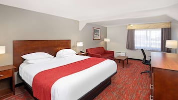 A hotel room with a large bed, a desk, a chair, and a window with curtains.