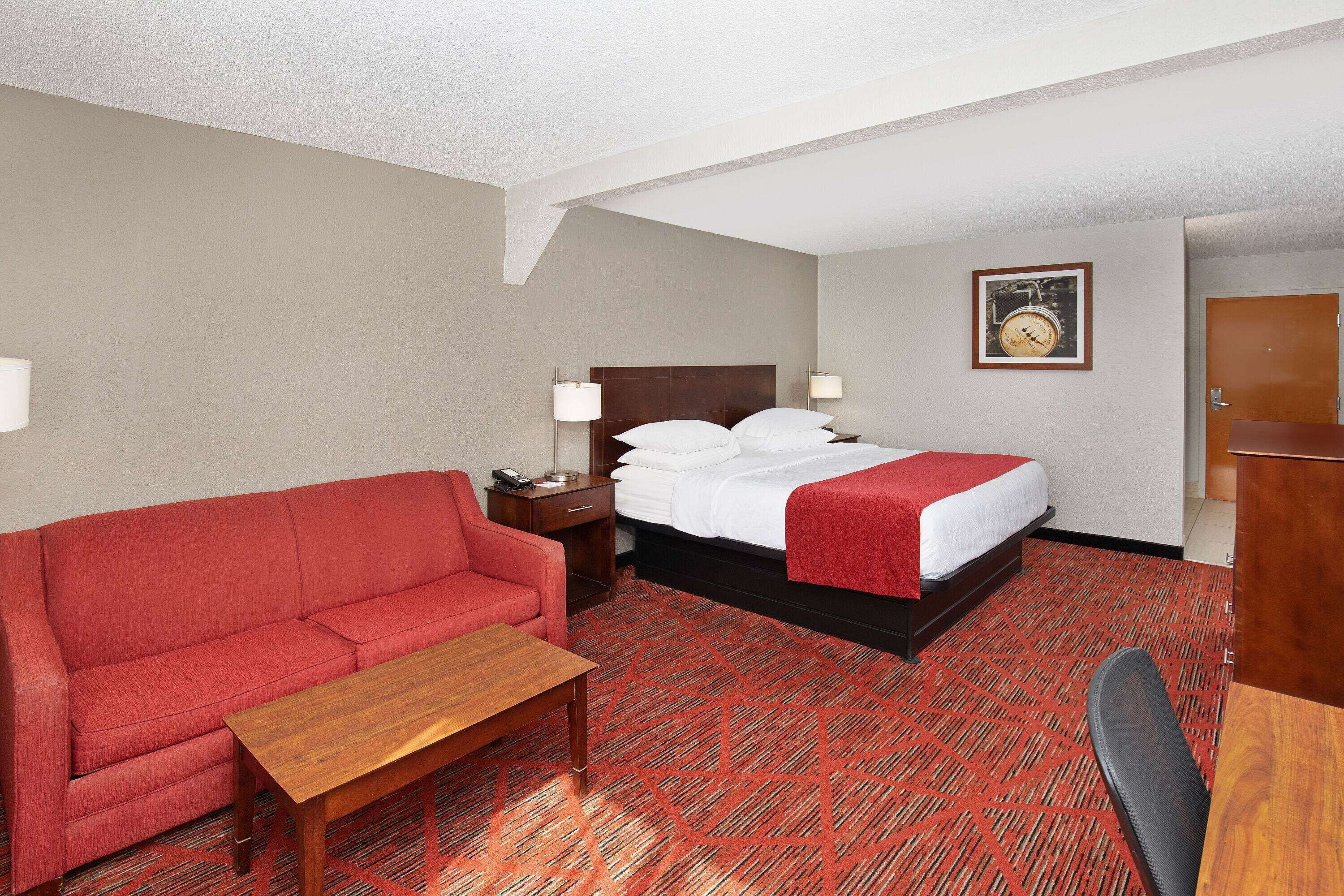 Une chambre d’hôtel avec un lit, un canapé rouge, une table en bois et un bureau.
