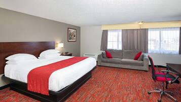 A hotel room with a large bed, a grey sofa, and a desk with a chair.