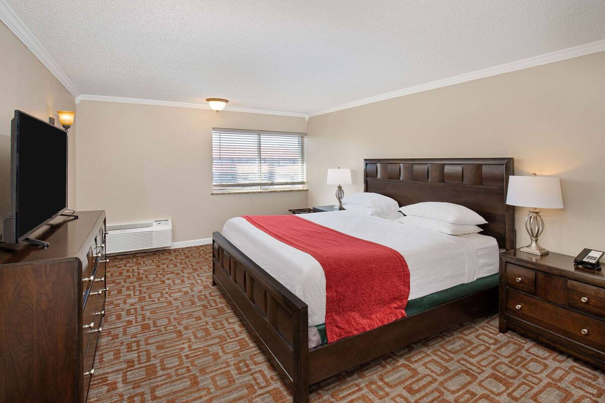Ett hotellrum med en stor säng, en byrå, en tv och ett fönster med persienner.