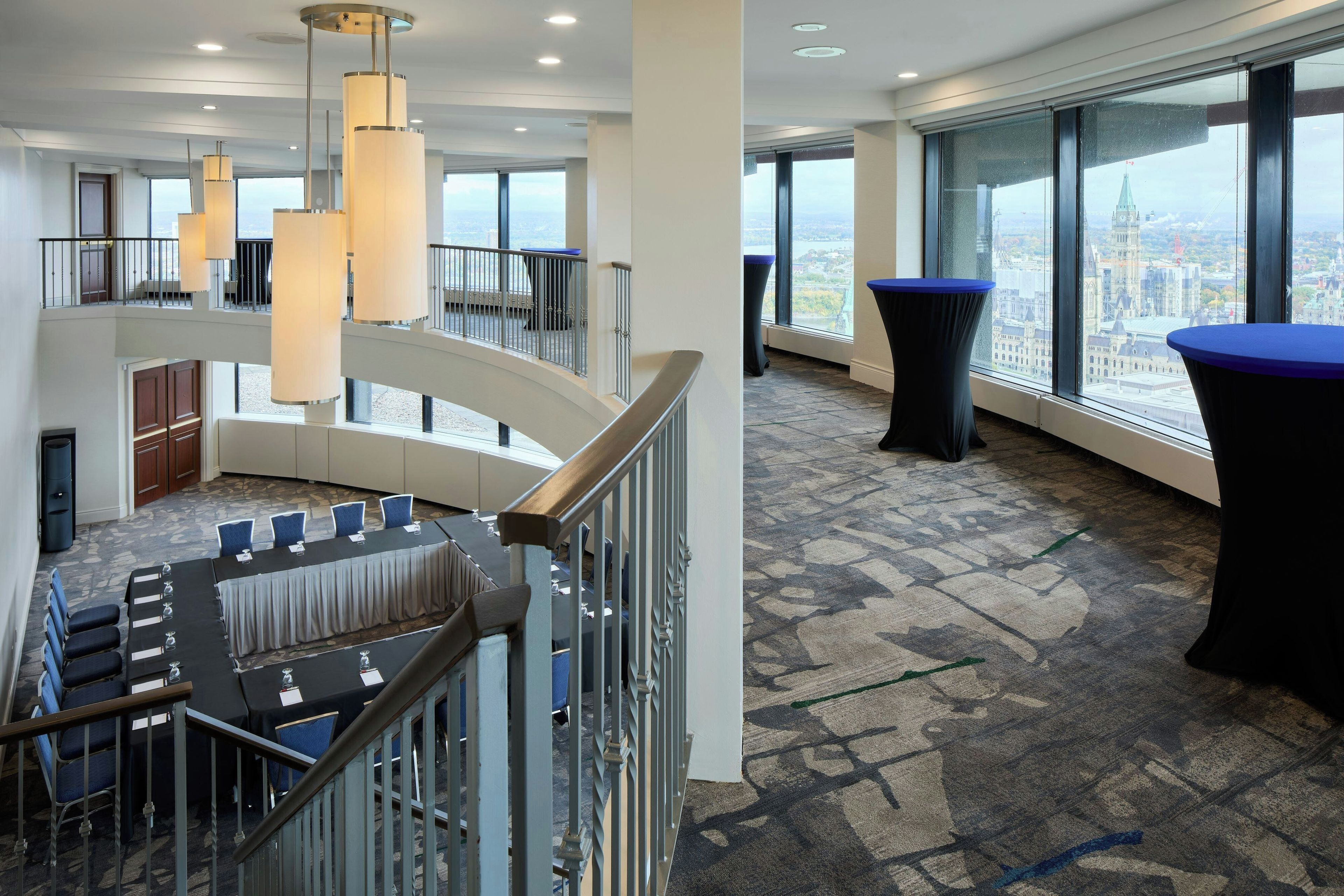 Un hall d’hôtel moderne avec un escalier en colimaçon, une table de conférence et une vue panoramique sur la ville.