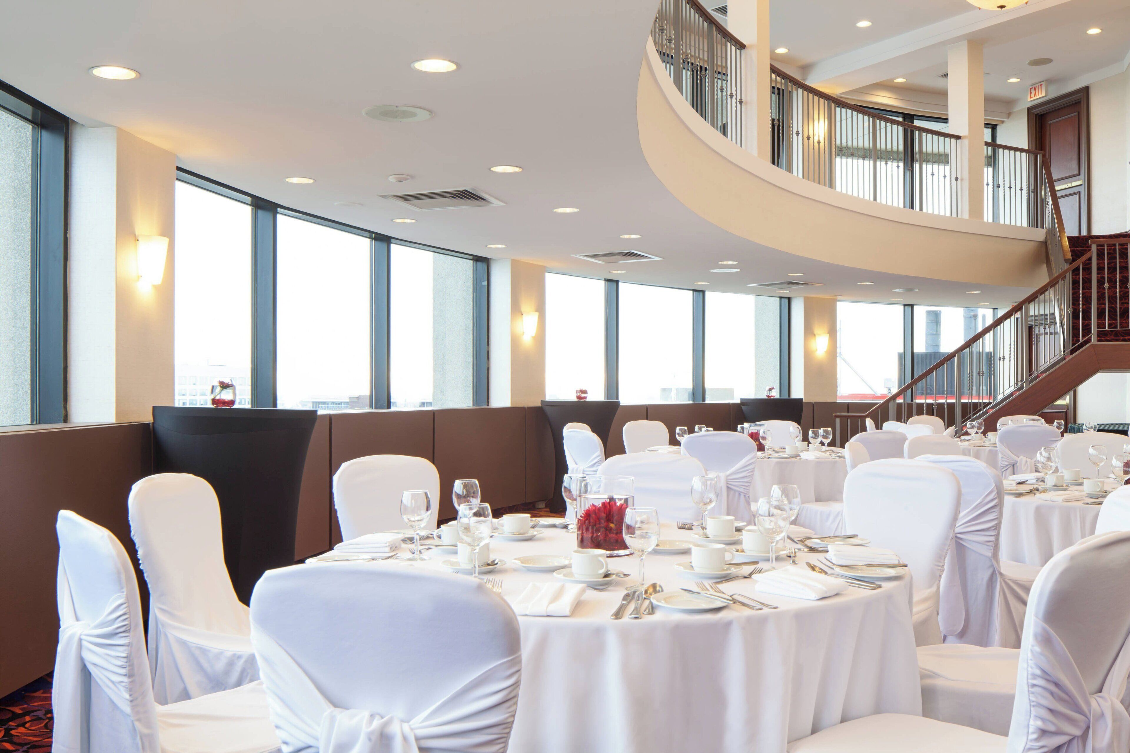 A conference room with round tables, white chairs, and a staircase.