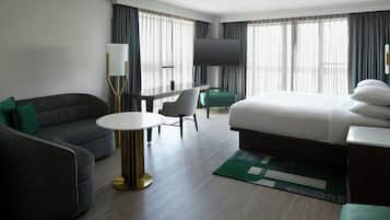 A hotel room with a bed, a desk, a sofa, a TV, and a window with curtains.