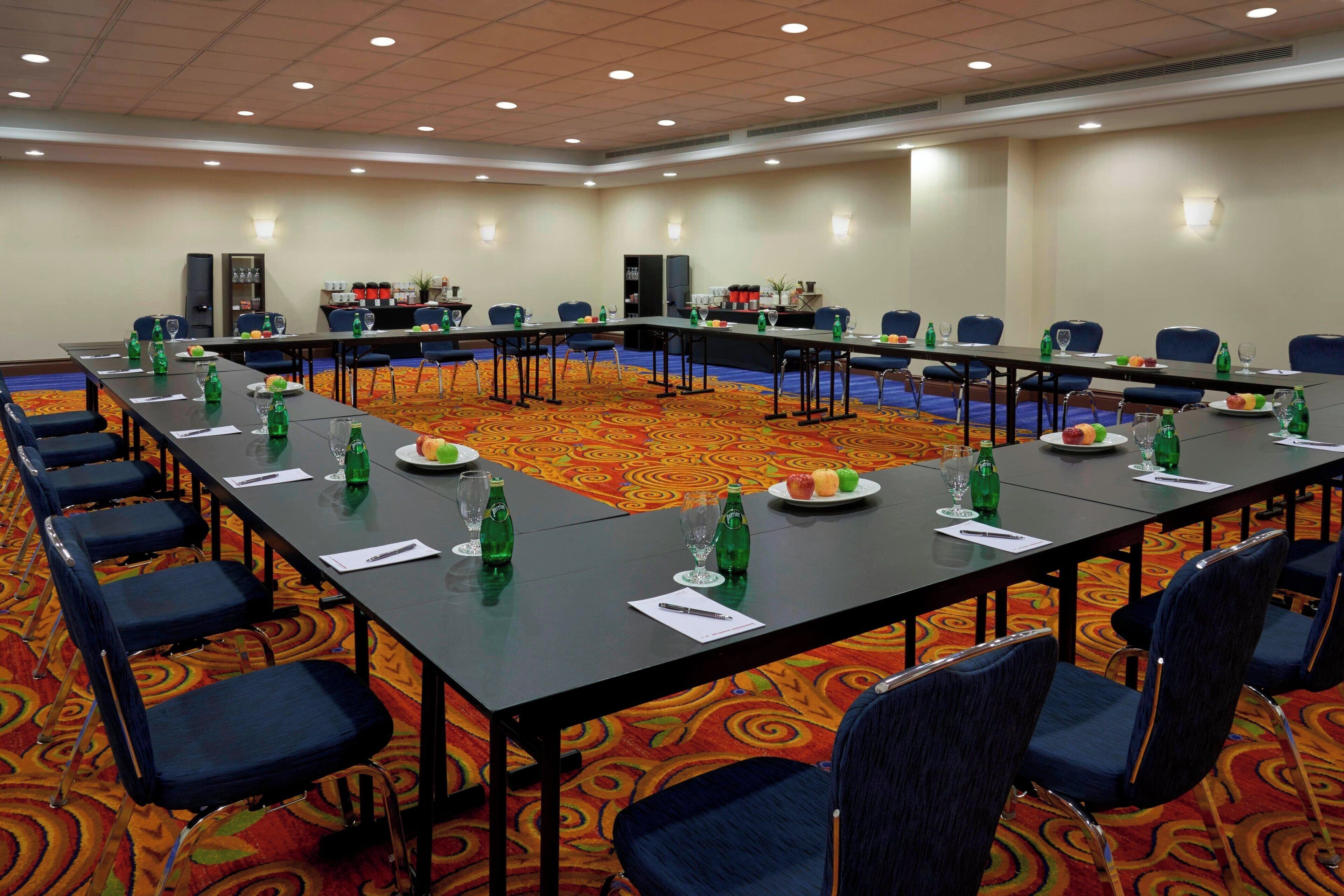 Un salón de conferencias con mesas largas, sillas y piso alfombrado.