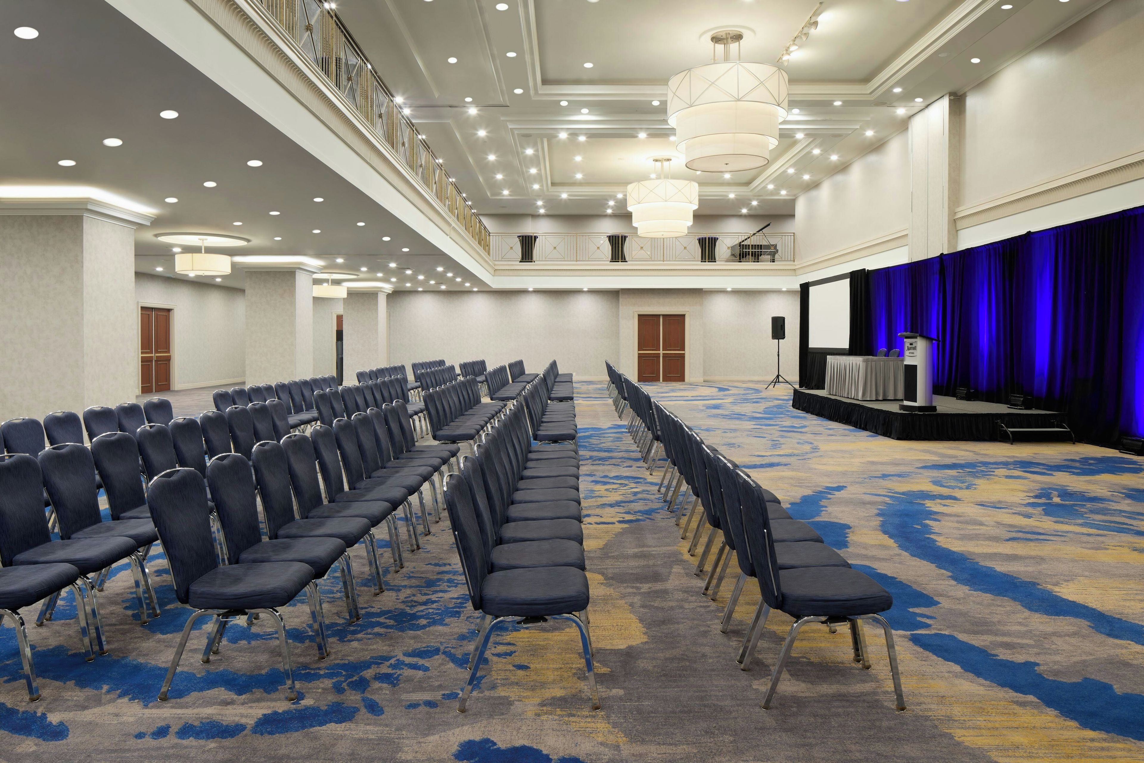 A conference room with rows of chairs, a stage with a blue curtain, and a balcony with railings.