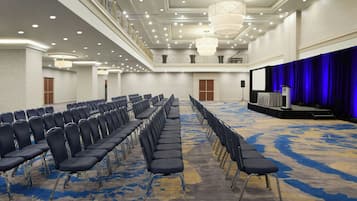 A conference room with rows of chairs, a stage with a blue curtain, and a balcony with railings.