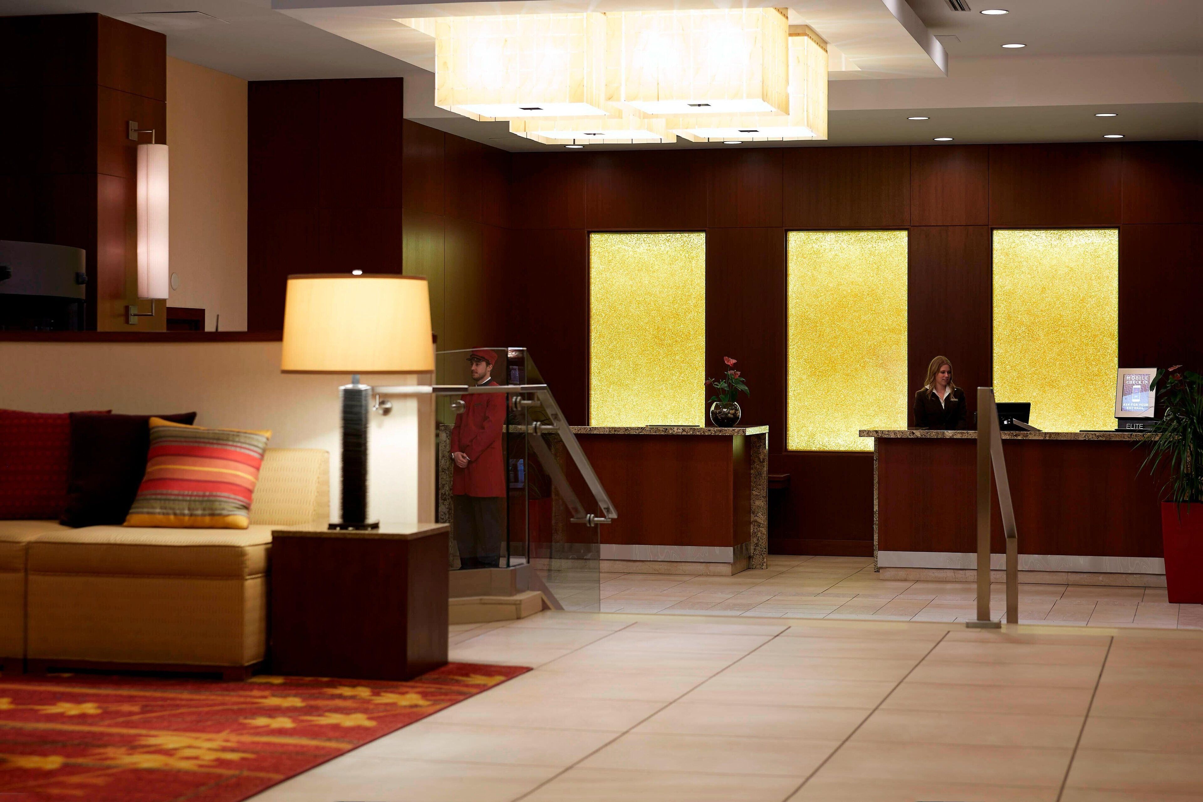 Un vestíbulo de hotel con mostrador de recepción, un sofá, una lámpara y una escalera.