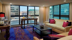 Habitación de hotel con un ventanal grande, un sofá, una mesa de centro y una alfombra estampada.